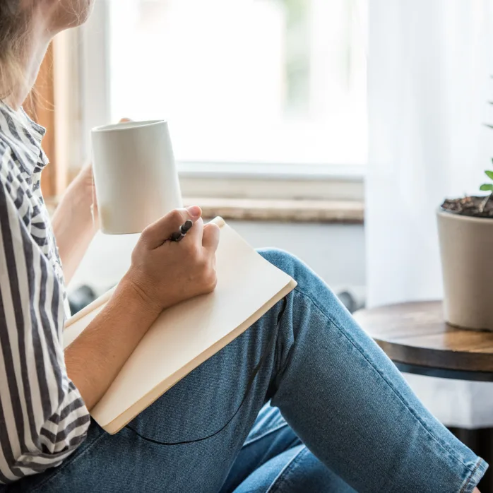 woman drinking coffee writing in notebook